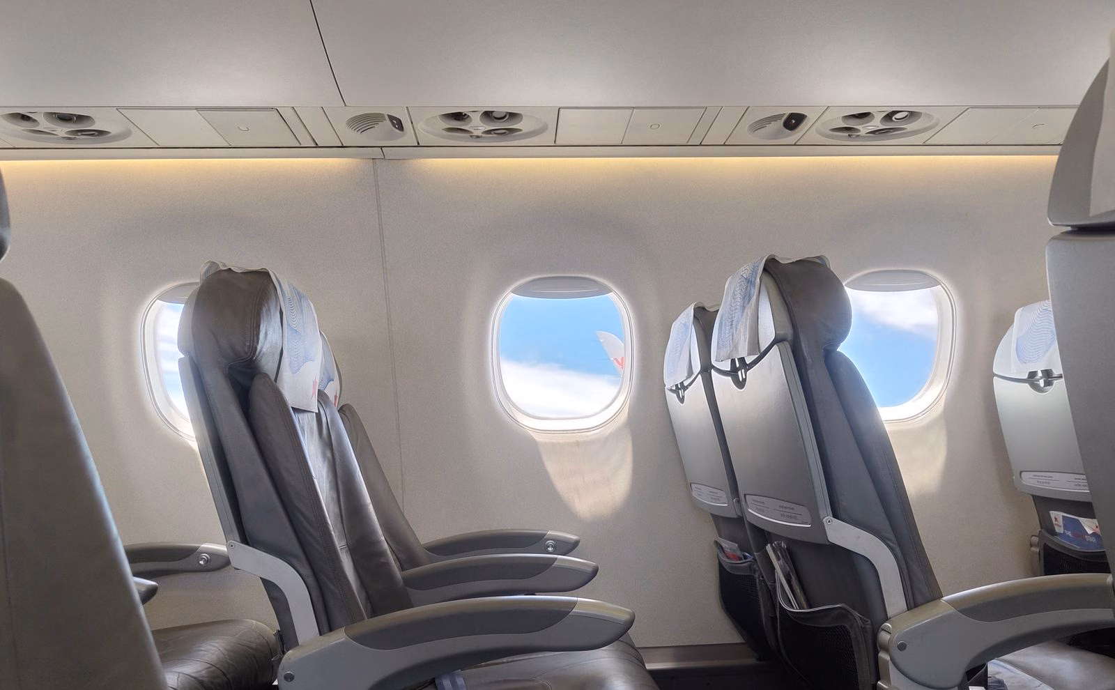 Rows of empty economy airplane seats stretching down a cabin with daylight coming through the windows