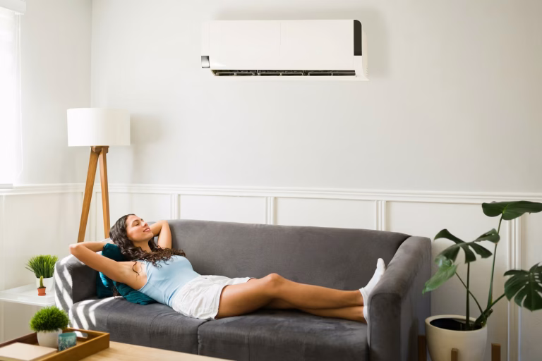 Woman relaxing on a gray sofa beneath a wall-mounted ductless mini-split