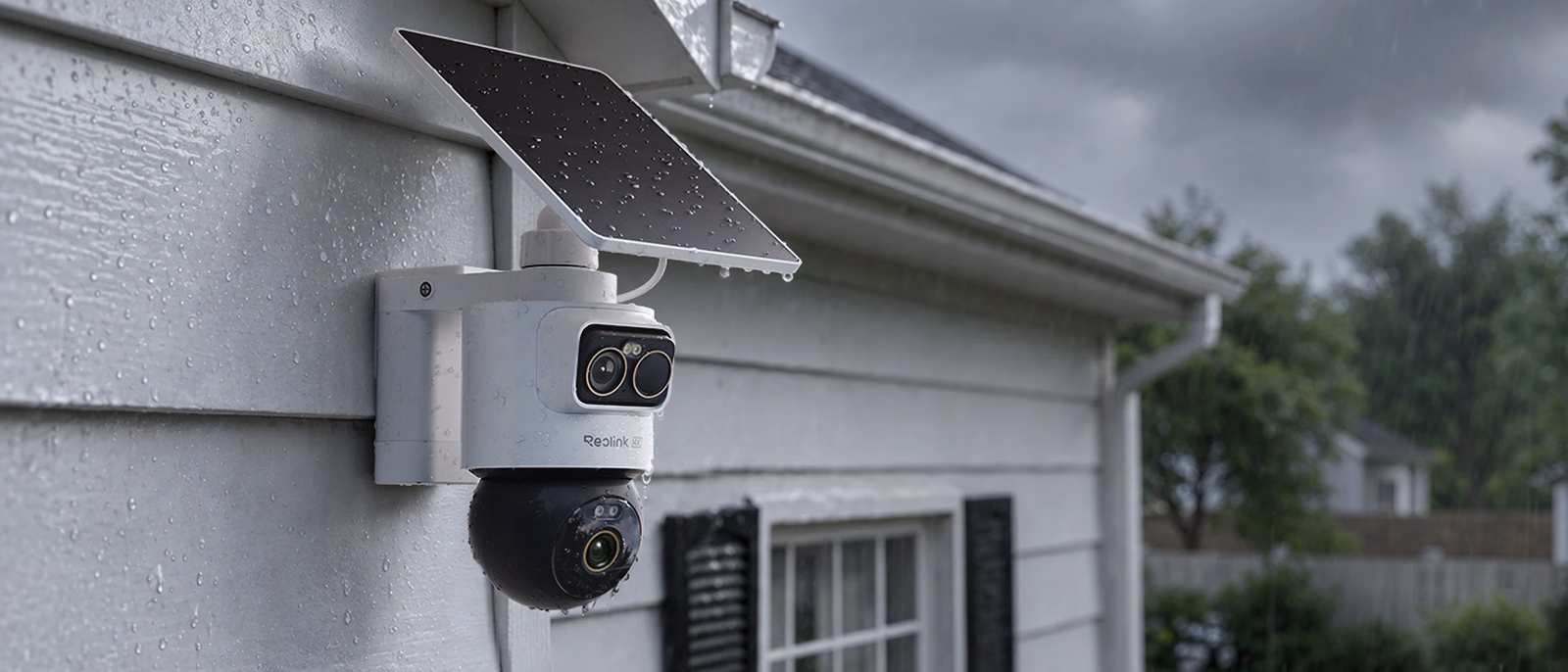 White Reolink OMVI 2i Ultra mounted under the eaves of a gray house in the rain, with its solar panel attached on top